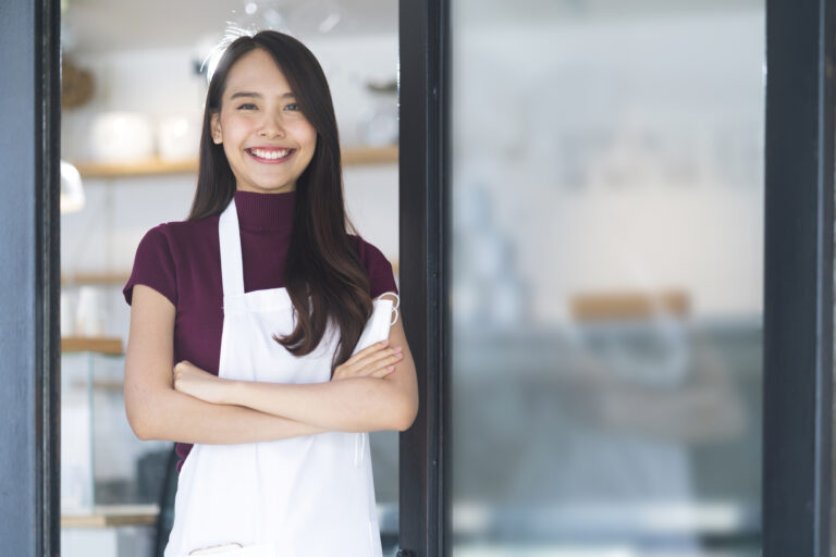 asian attractive female cafe staff wear uniform apron smiling cheerful welcome to cafe reataurant with confident and happiness with positive service mind after lockdown is over in shopfront entrance